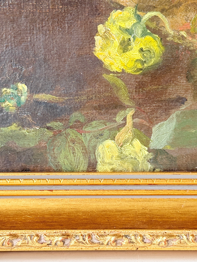 Close-up of a framed painting showing yellow flowers and green leaves against a dark brown background, with an ornate gold frame visible at the bottom.