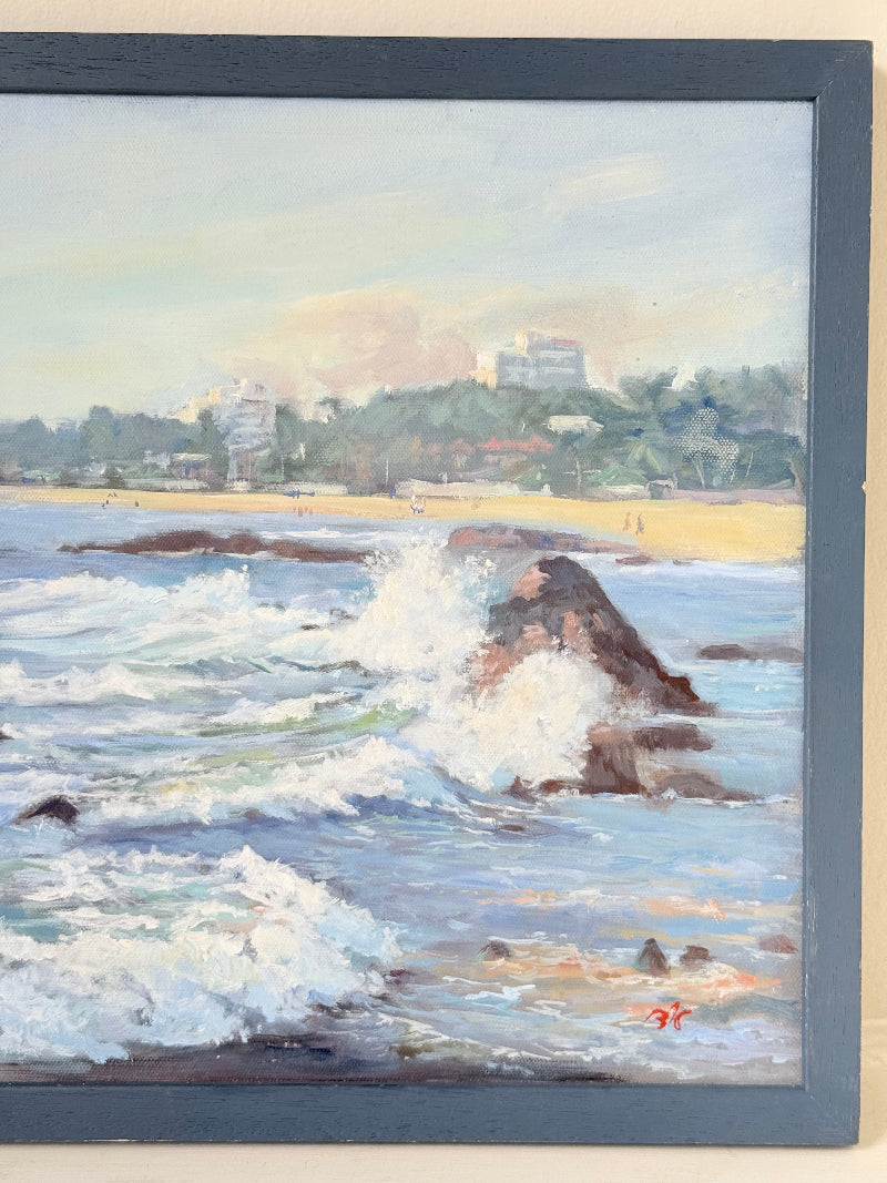 Original oil painting of waves crashing against rocks, signed seascape in slate blue wooden frame on white surface