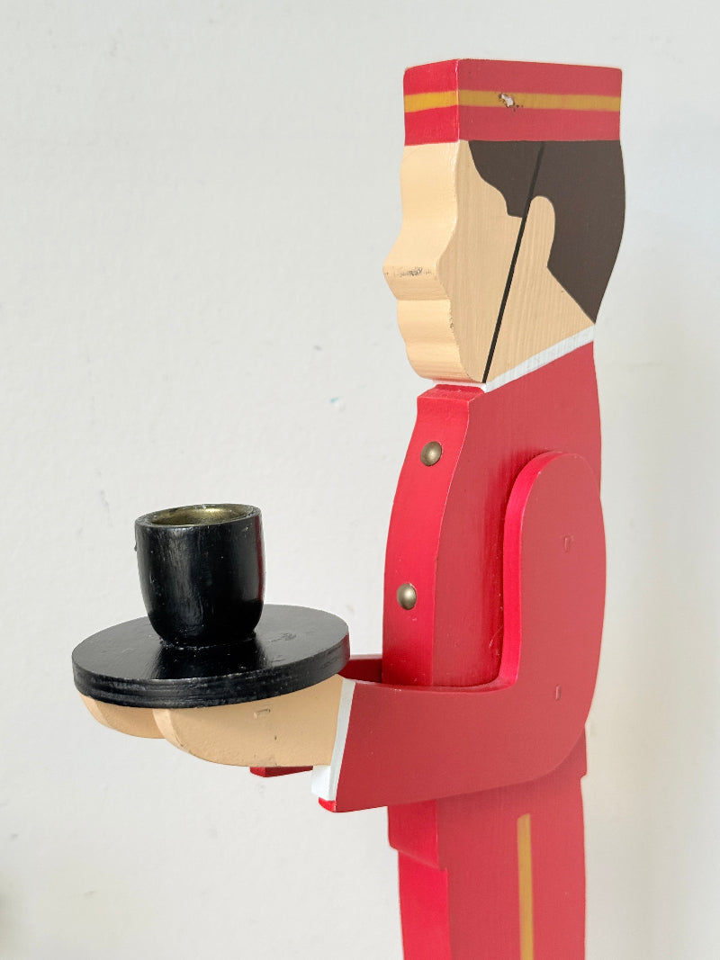 Vintage bellboy candlestick holder in red and black holding a tray with candle, photographed on a white surface