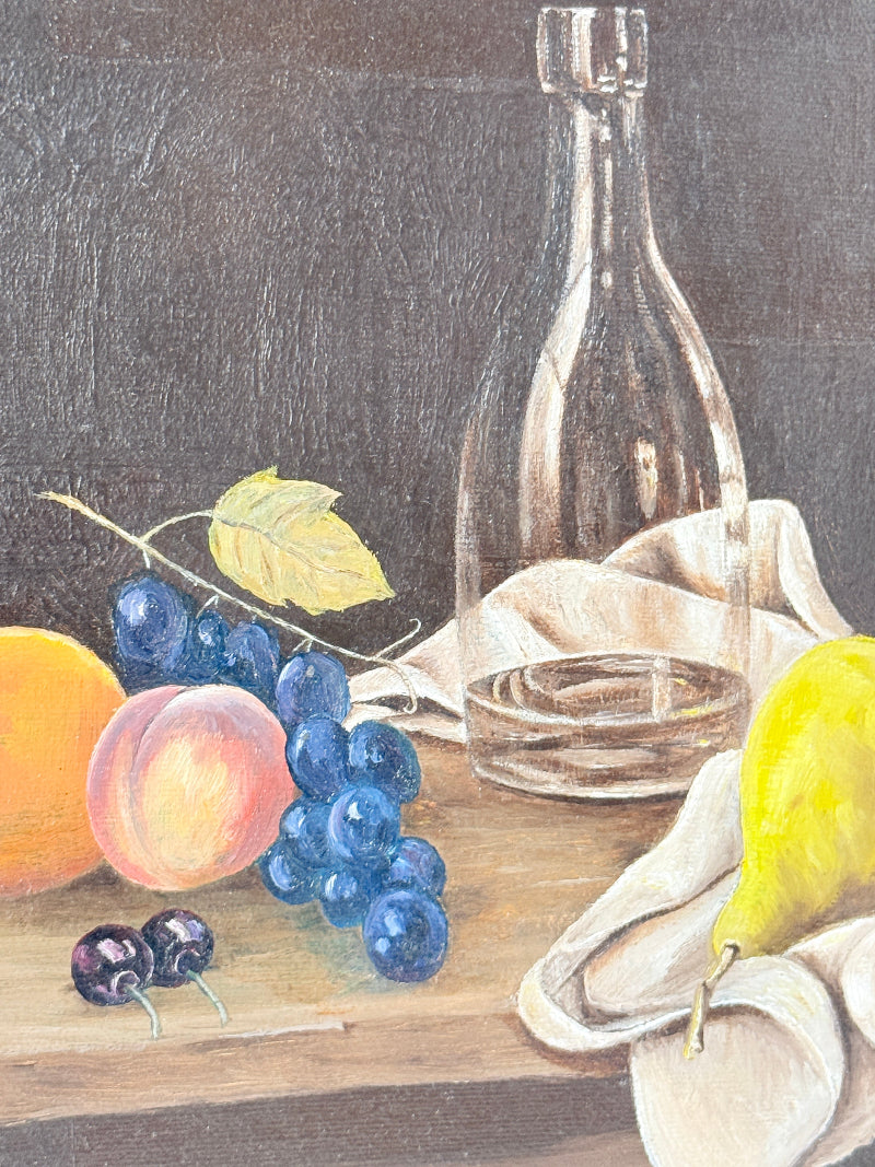A still life painting featuring a clear glass bottle, blue grapes, a peach, an orange, a yellow pear, and two dark cherries on a wooden surface with a draped white cloth against a dark gray background.