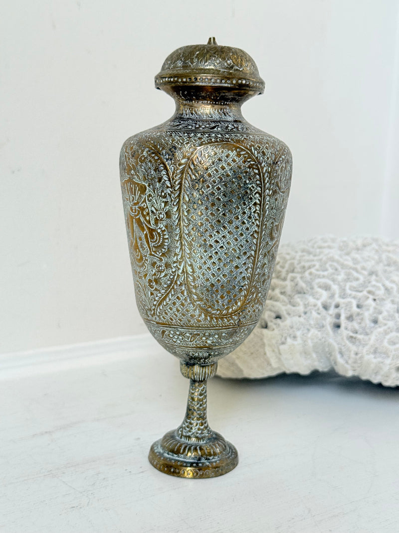 Indian Benares brass lidded vase with engraved figures and pedestal base, photographed on a white surface
