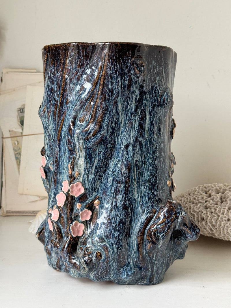 Large ceramic tree trunk vase with applied pink cherry blossom detail, textured bark form and dark drip glaze