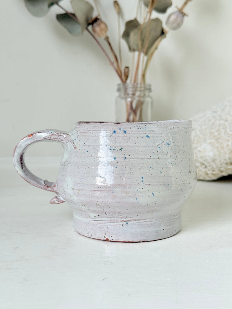 Studio pottery milk jug with soft pink and grey speckled glaze, photographed on a white surface