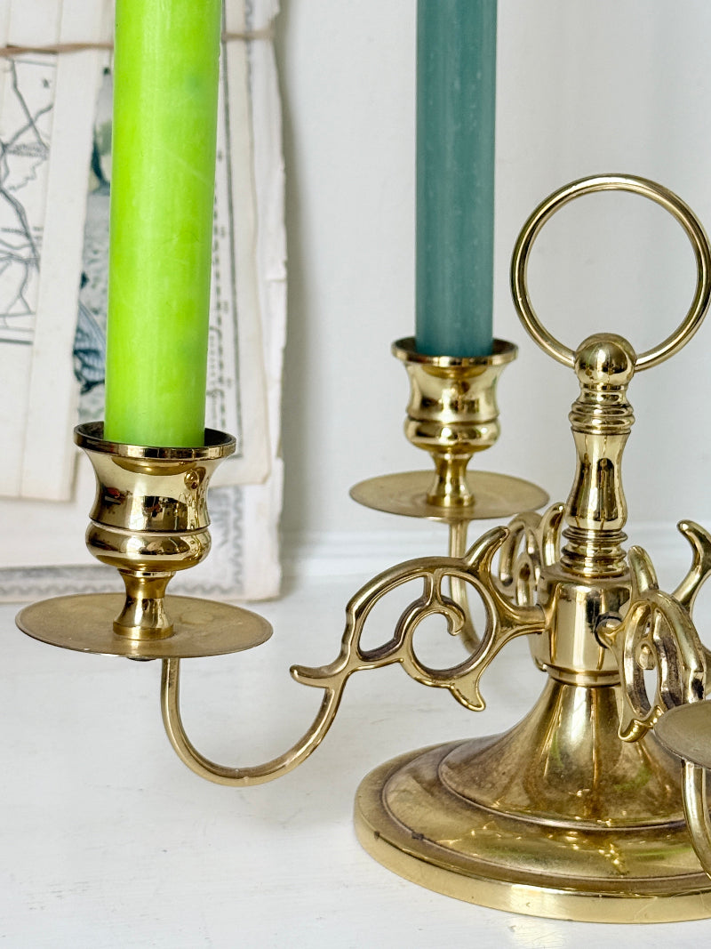 Brass five light candelabra with scrolled arms and a central ring handle on a domed base, photographed on a white surface
