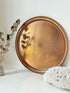 Lakeland Borrowdale hammered copper tray with warm patina, photographed on a white surface beside dried stems.