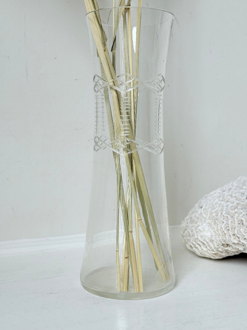 Vintage clear glass cylinder vase with etched leaf design, photographed on a white surface.