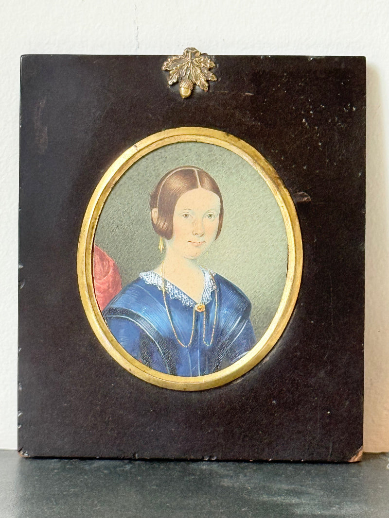 19th century watercolour miniature portrait of woman in blue dress, oval ebonised frame, styled on white background