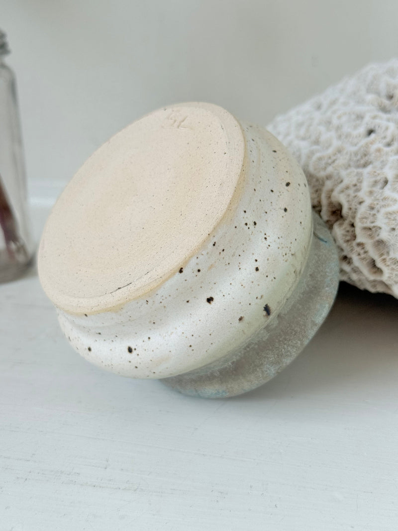 Studio pottery olive pot with soft green and cream glaze, photographed on a white surface