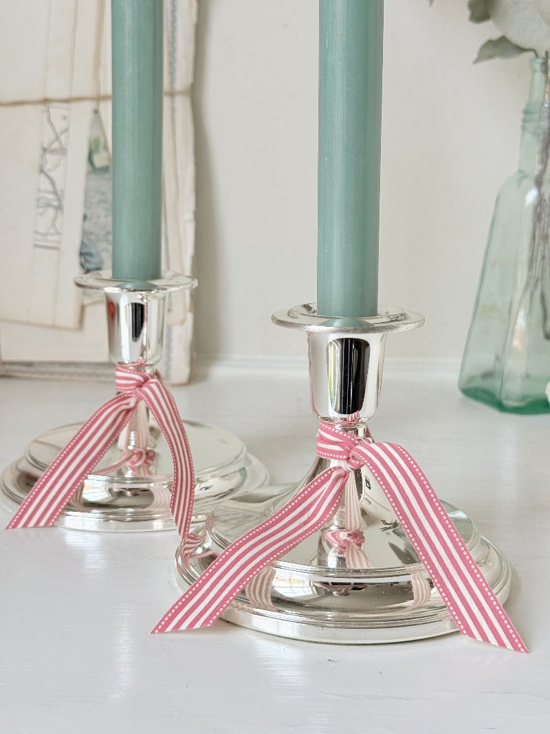 Pair of silver tone candlesticks with wide round stepped bases holding green candles, photographed on a white surface