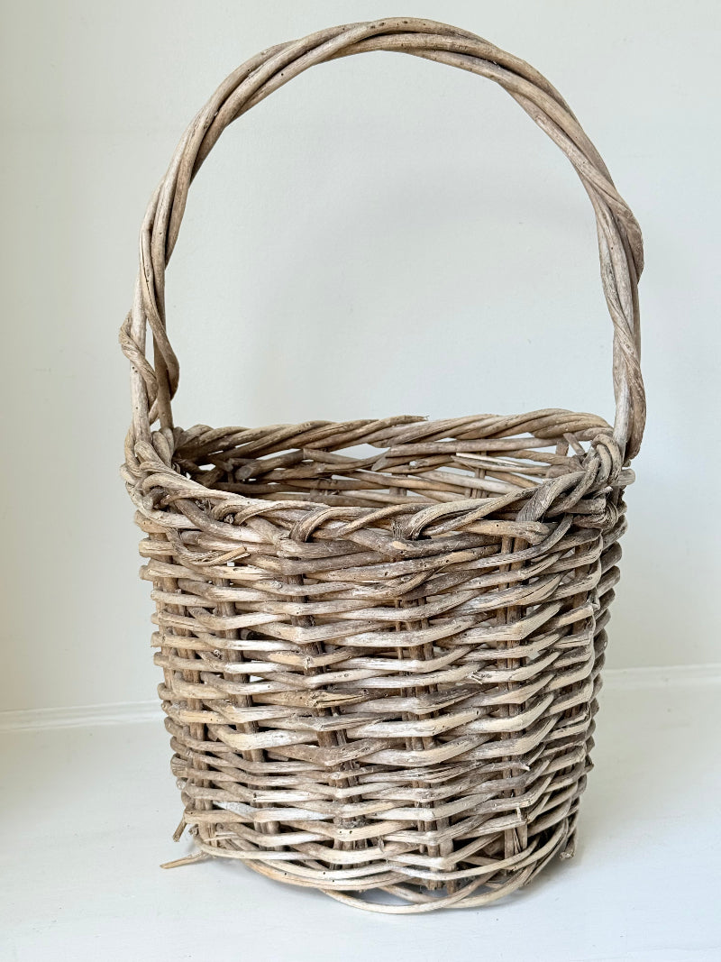 Rustic vintage wicker basket with woven handle and aged natural finish photographed on a white surface