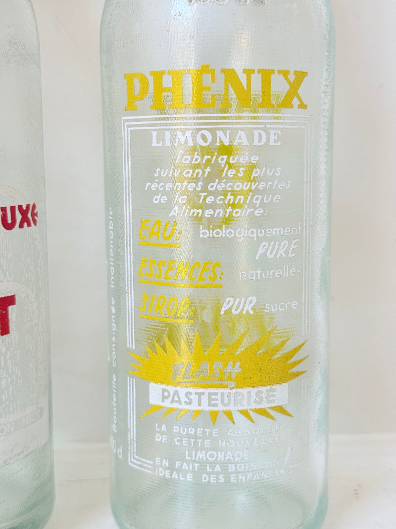 Pair of vintage French glass bottles with retro typography and graphics, photographed on a white surface