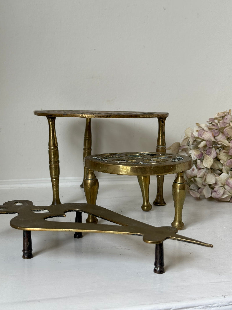Vintage brass trivet trio with ornate cutwork designs and aged patina, photographed on a white surface