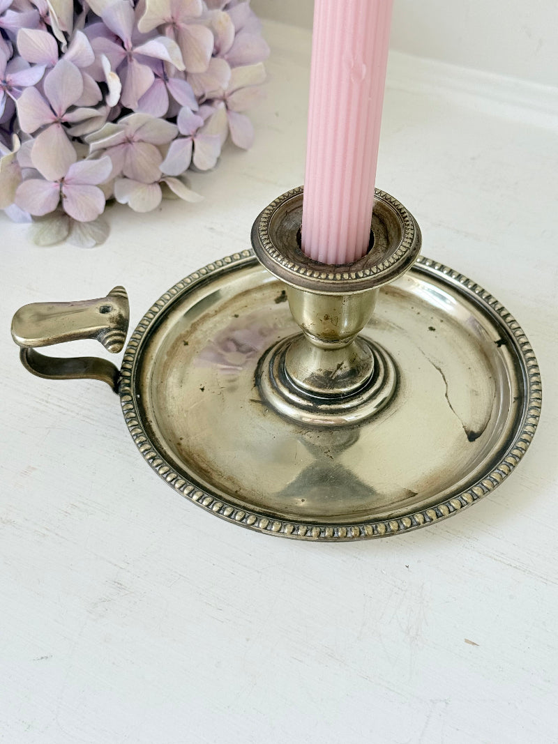 Antique silver plate chamberstick with handle, photographed on a white surface beside pink hydrangeas and vintage books