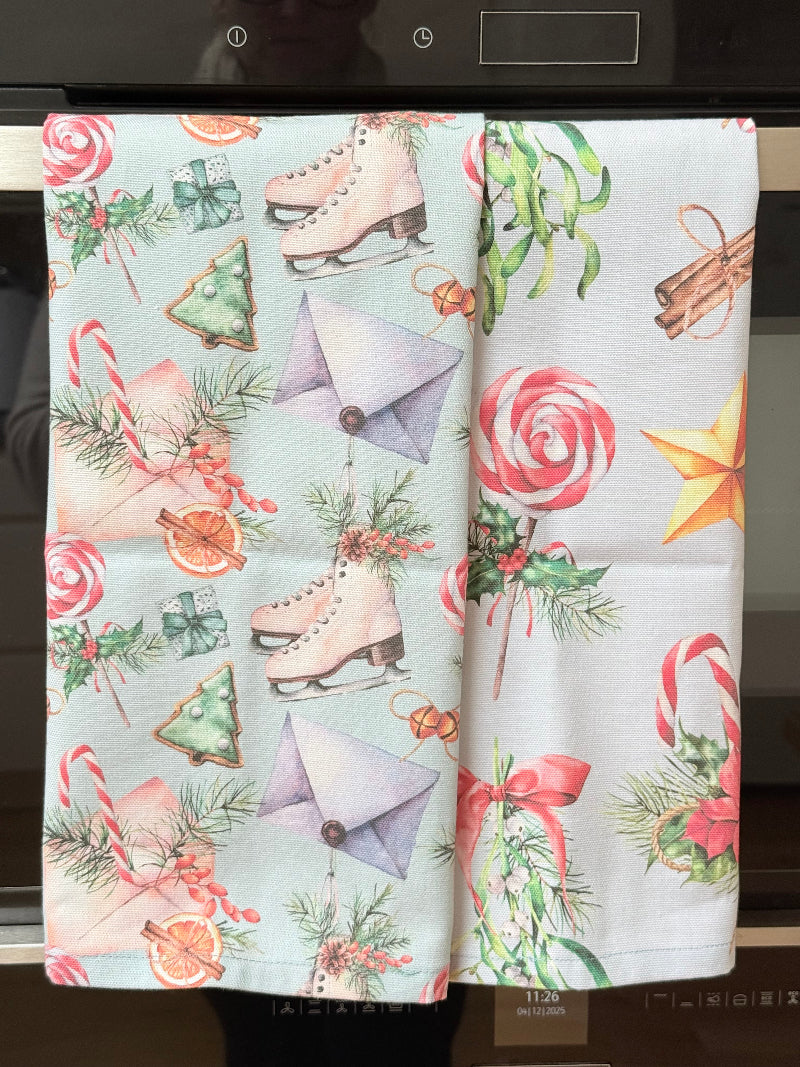 Pair of pastel blue festive tea towels with candy cane and ribbon print, folded, photographed on a kitchen worktop