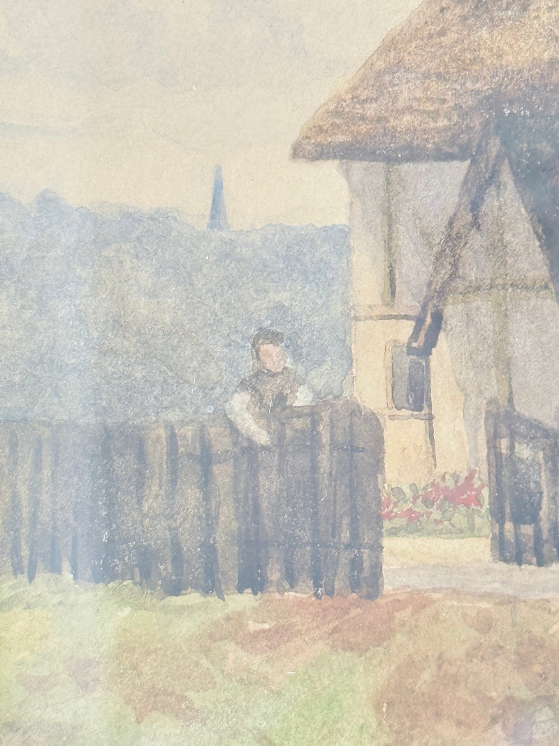 Antique framed watercolour of English village street with thatched cottages and figures, in gilt frame with wide mount, on white surface.