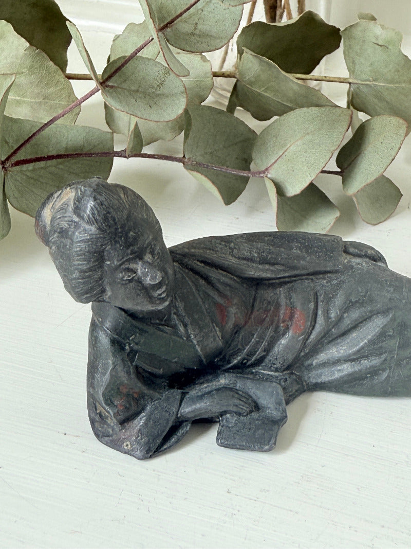antique japanese bronze reclining lady with impressed marks to base photographed on white surface with foliage background