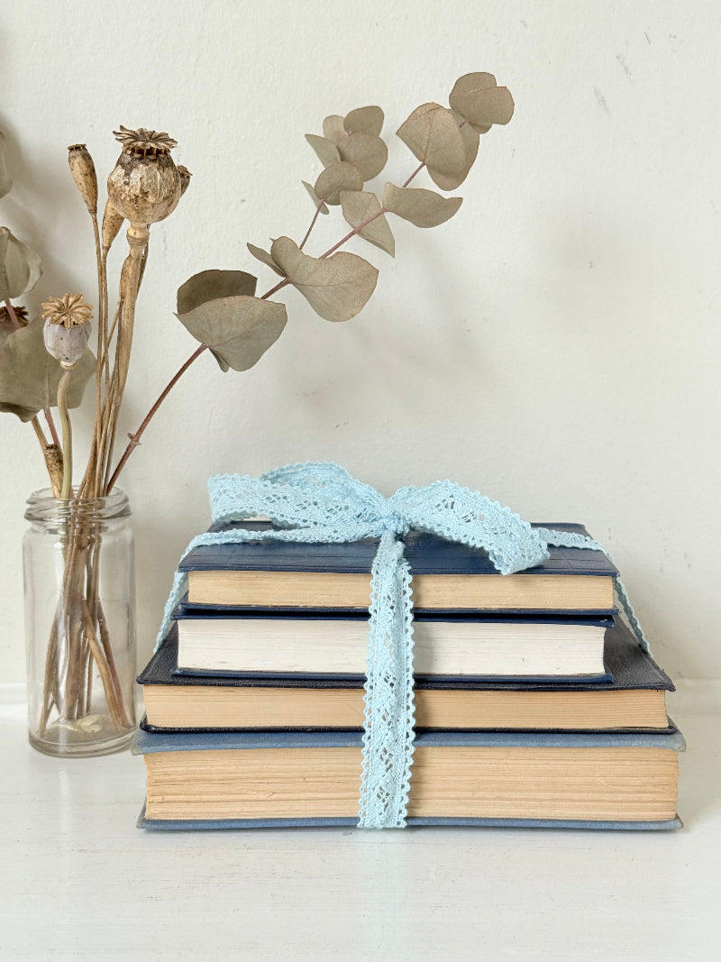 Vintage navy decorative book bundle tied with pale blue lace ribbon, photographed on a white surface