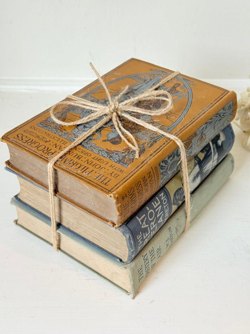Vintage decorative book bundle in blue, grey, and ochre tied with twine, photographed on a white surface