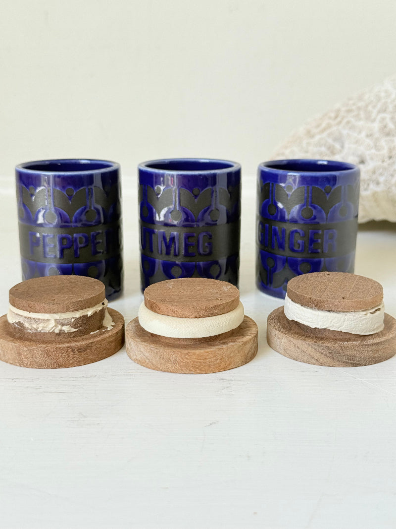 Set of three Hornsea Pottery spice jars in cobalt blue with wooden lids, labelled Ginger, Nutmeg, and Peppercorn, photographed on white surface