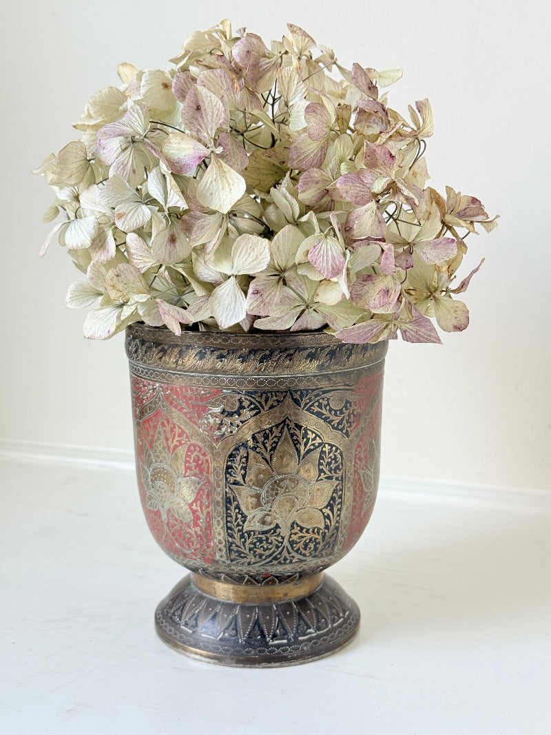 vintage indian metal lassi cup with red and white enamel motifs, styled with dried hydrangeas on a white surface