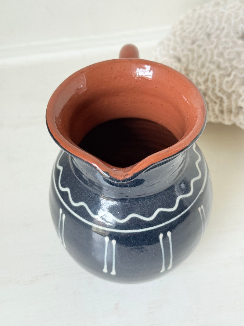 Slipware studio pottery jug with blue glaze and terracotta handle, photographed on a white surface