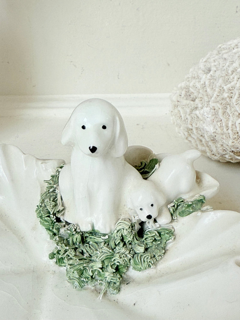 Italian ceramic dish featuring two white dogs on a sculpted leaf base, photographed on a white surface.
