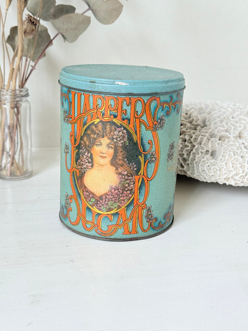 Vintage turquoise and gold metal sweet tin with Art Nouveau woman portrait photographed on a white surface.