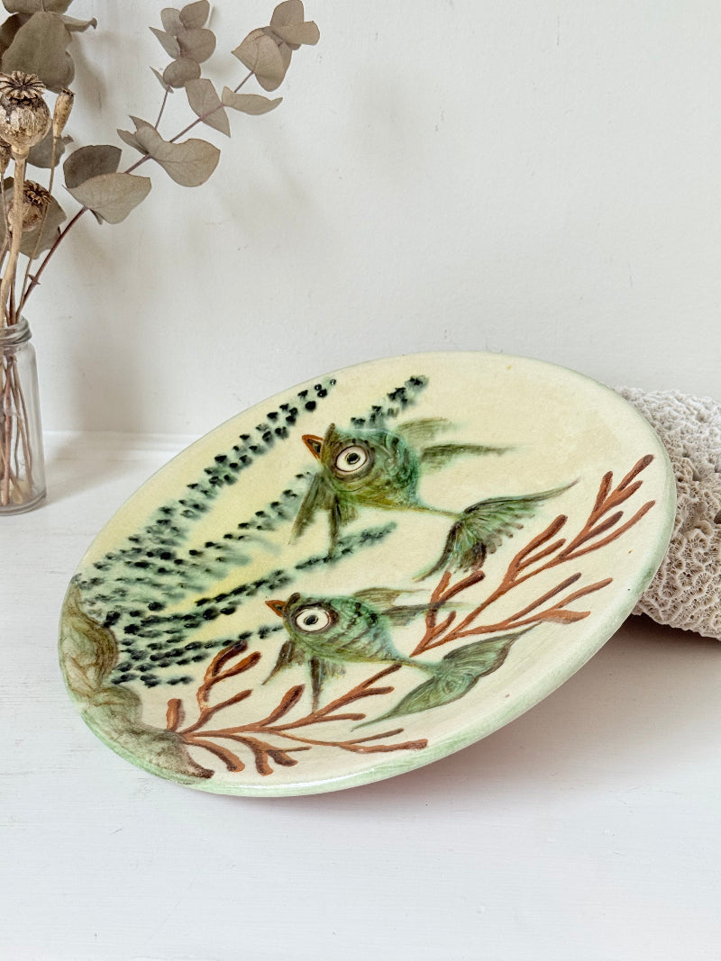 Puidgemont Spanish studio pottery plate with hand painted fish and coral design in green, turquoise, and terracotta tones, photographed on a white surface.