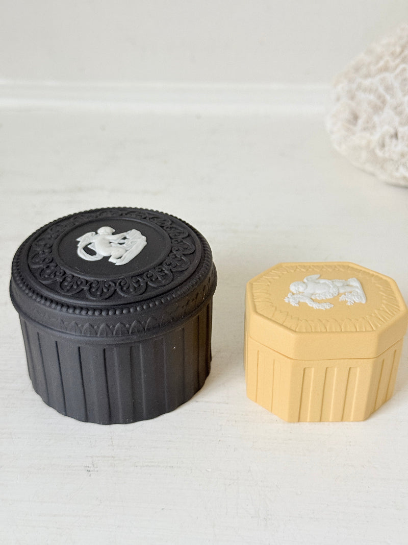Pair of vintage Wedgwood Jasperware trinket pots in black and yellow with white relief decoration, photographed on a white surface