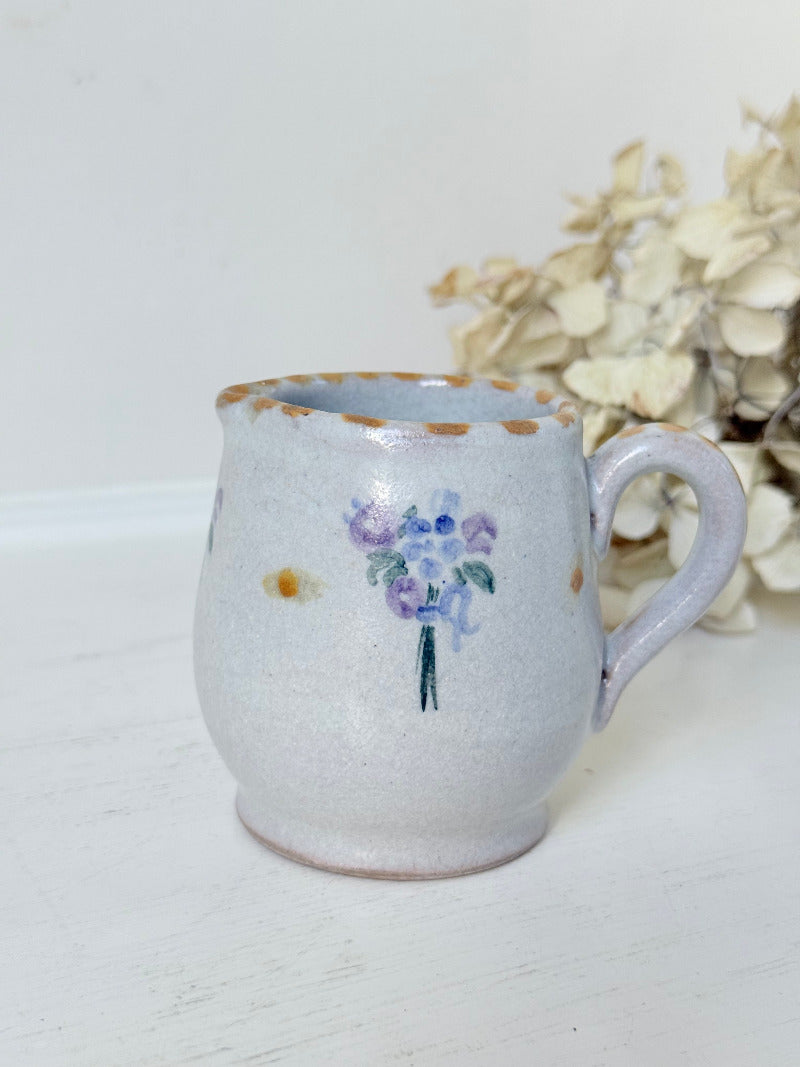 vintage studio pottery milk jug with hand painted lilac flowers and ochre rim photographed on white surface