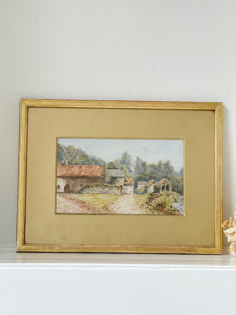 Framed vintage watercolour of countryside farm buildings with red roofs in gold frame photographed on a white surface