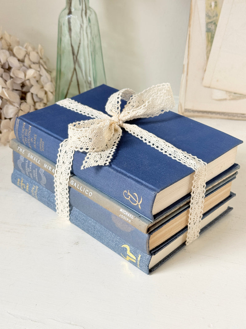 Bundle of vintage blue cloth books with gilt spines tied with ivory lace ribbon for shelf and table styling