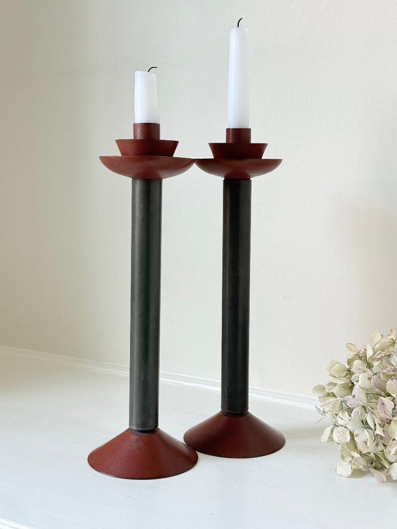 Pair of tall vintage metal candlesticks in black and burgundy, styled with white taper candles on a white surface.