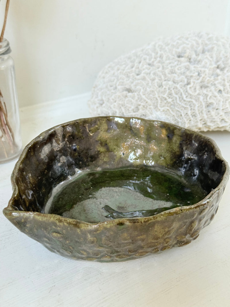 Studio pottery olive bowl with green and charcoal glaze, photographed on a white surface