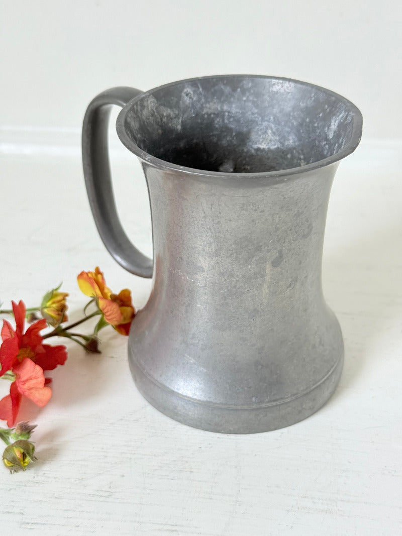 vintage pewter tankard with crown and rose mark and handle, styled with red and orange flowers on white surface