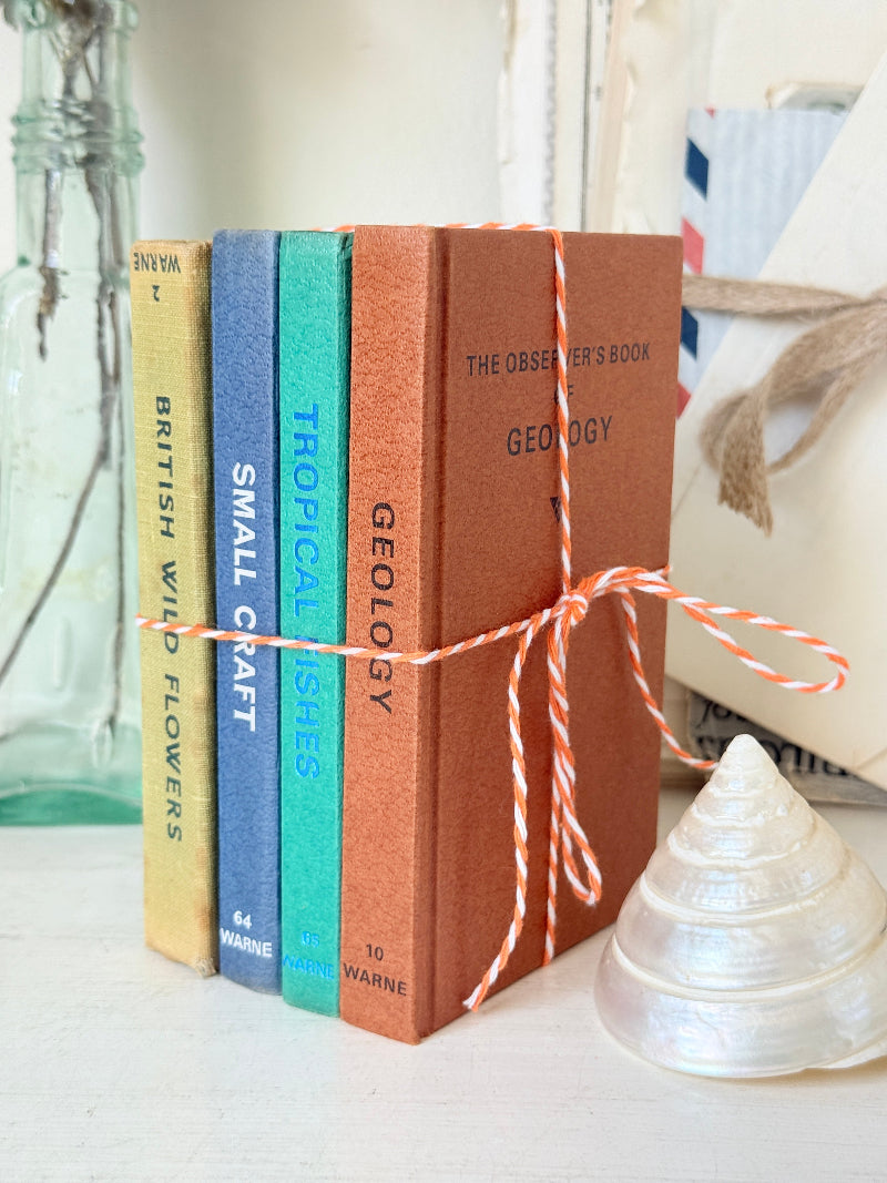 Four small hardcover books tied together with orange-and-white string, standing upright on a tabletop. The spines read &