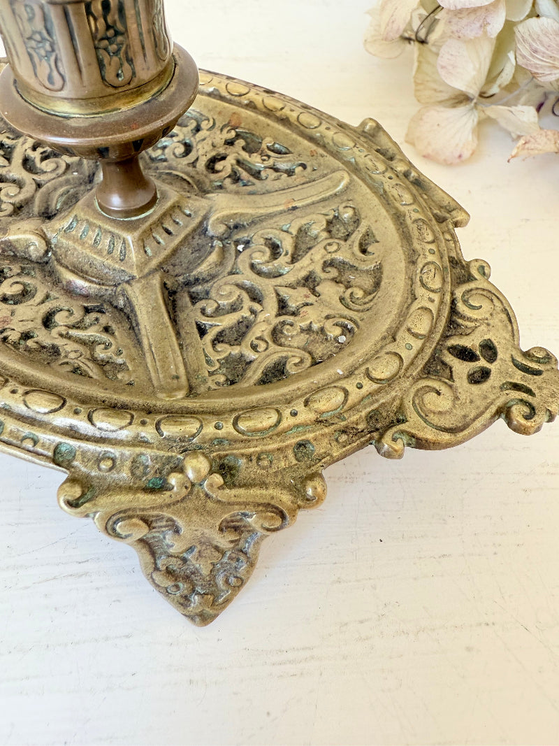 Ornate vintage brass candlestick with decorative handle and footed base, photographed on a white surface