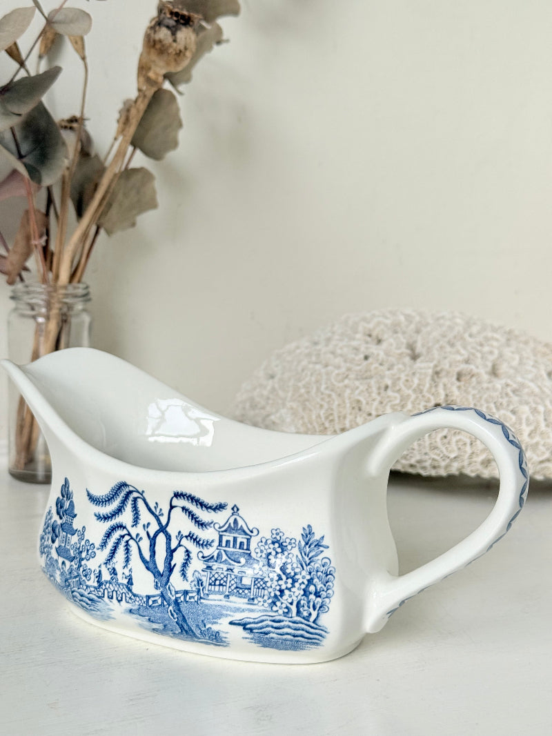 Vintage blue and white ceramic sauce boat with willow pattern photographed on a white surface