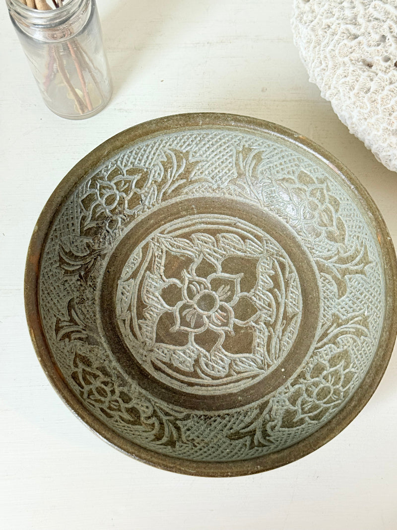 Studio pottery bowl with carved floral and geometric decoration in neutral glaze, photographed on a white surface with a pear inside.