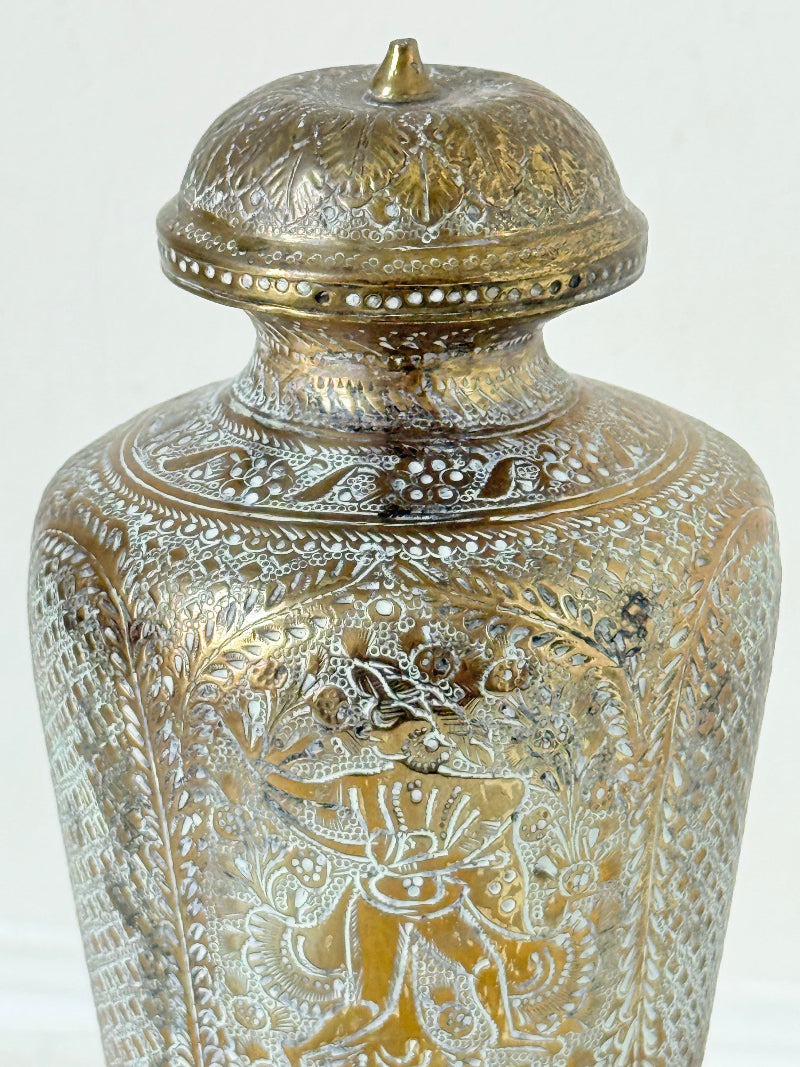 Indian Benares brass lidded vase with engraved figures and pedestal base, photographed on a white surface