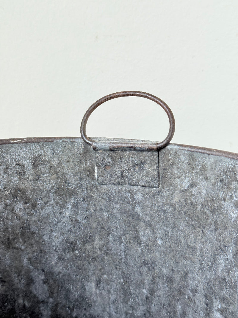 Vintage galvanised metal bin with handles, photographed on a white surface.