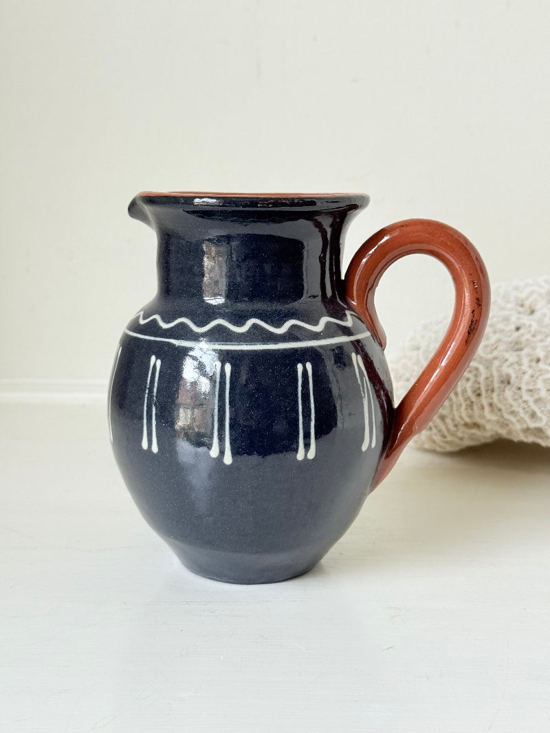 Slipware studio pottery jug with blue glaze and terracotta handle, photographed on a white surface