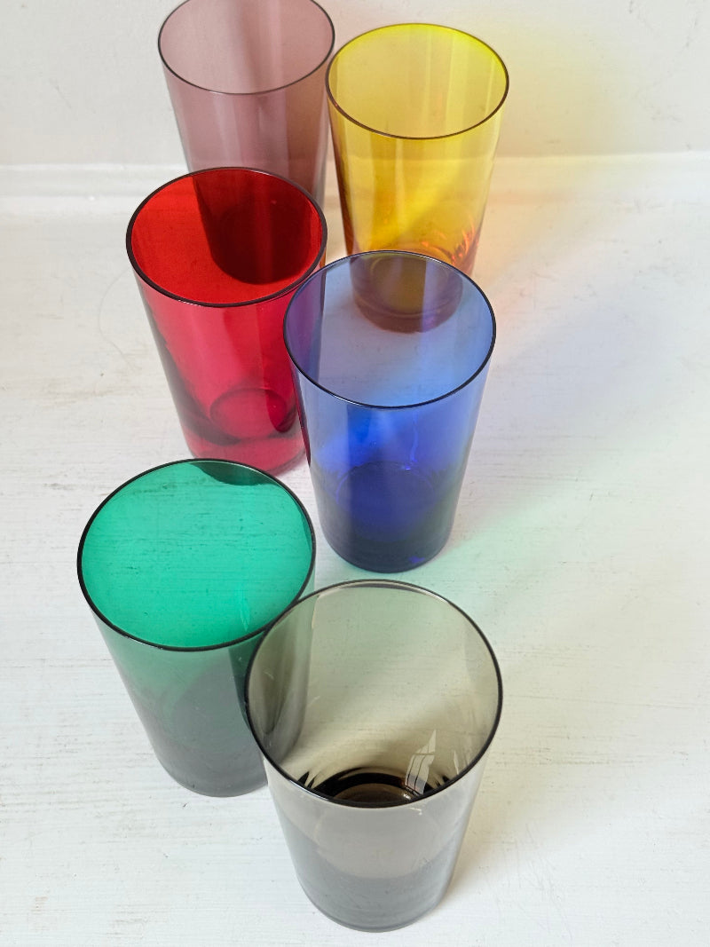 Set of six mid-20th century Boussu coloured glass beakers in rainbow hues, green with original label, photographed on white surface.