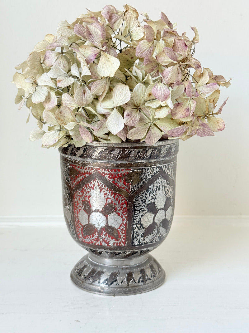 vintage indian metal lassi cup with red and white enamel motifs, styled with dried hydrangeas on a white surface