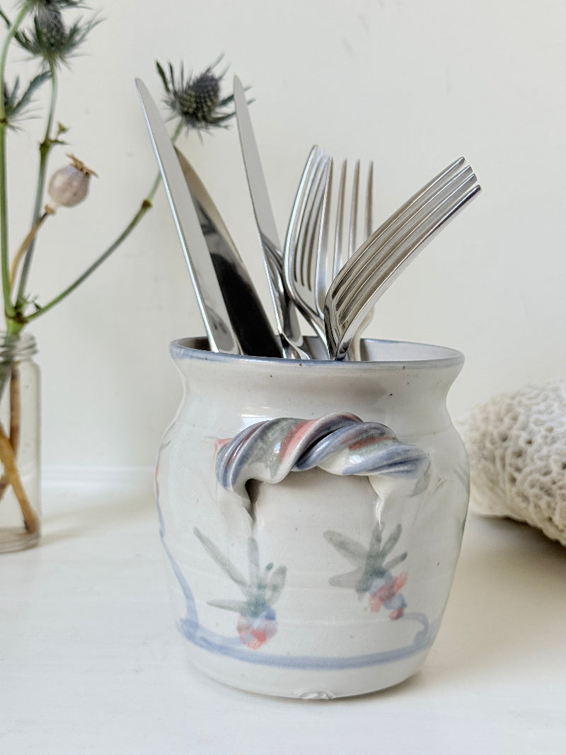 Vintage studio pottery utensil pot with hand painted floral decoration and applied handle detail, photographed on a white surface