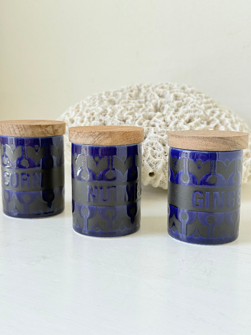 Set of three Hornsea Pottery spice jars in cobalt blue with wooden lids, labelled Ginger, Nutmeg, and Peppercorn, photographed on white surface