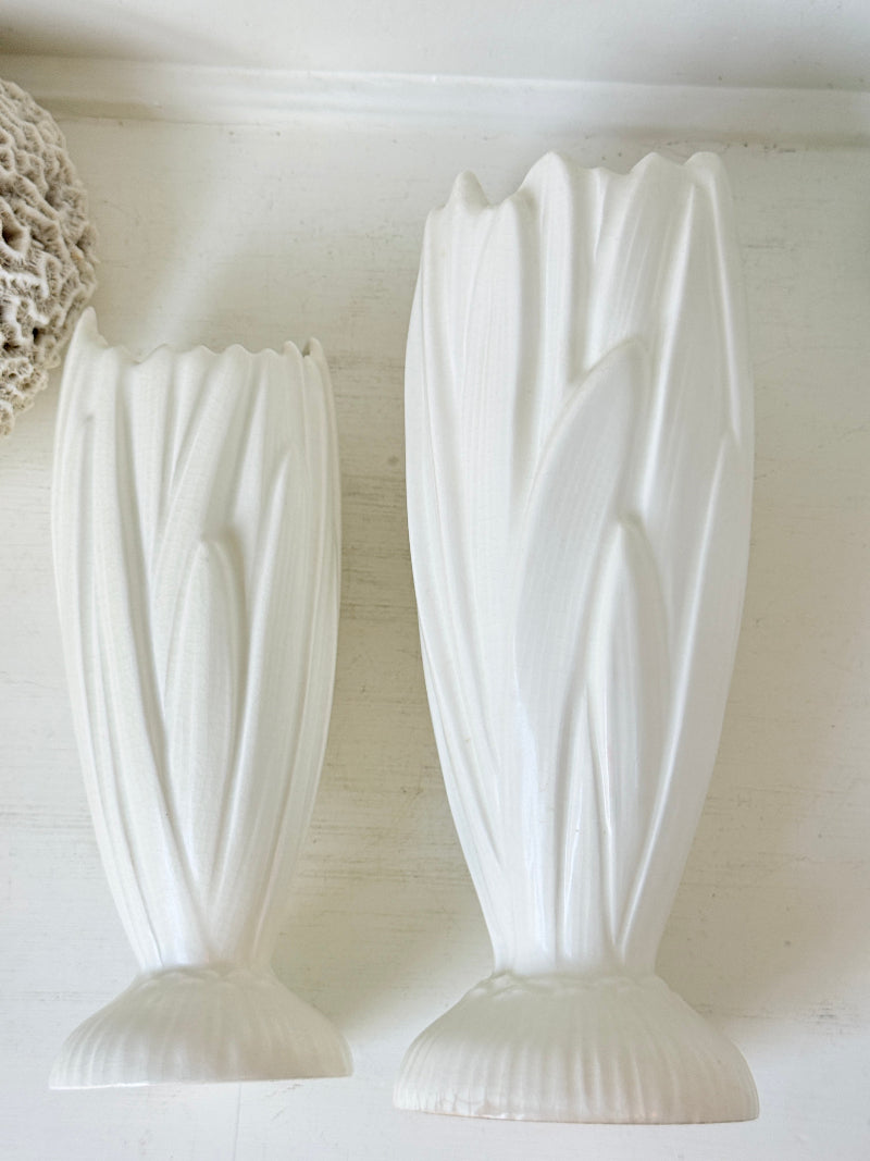 Two white ribbed ceramic vases with a tulip-like flared shape, displayed against a light off-white wall.