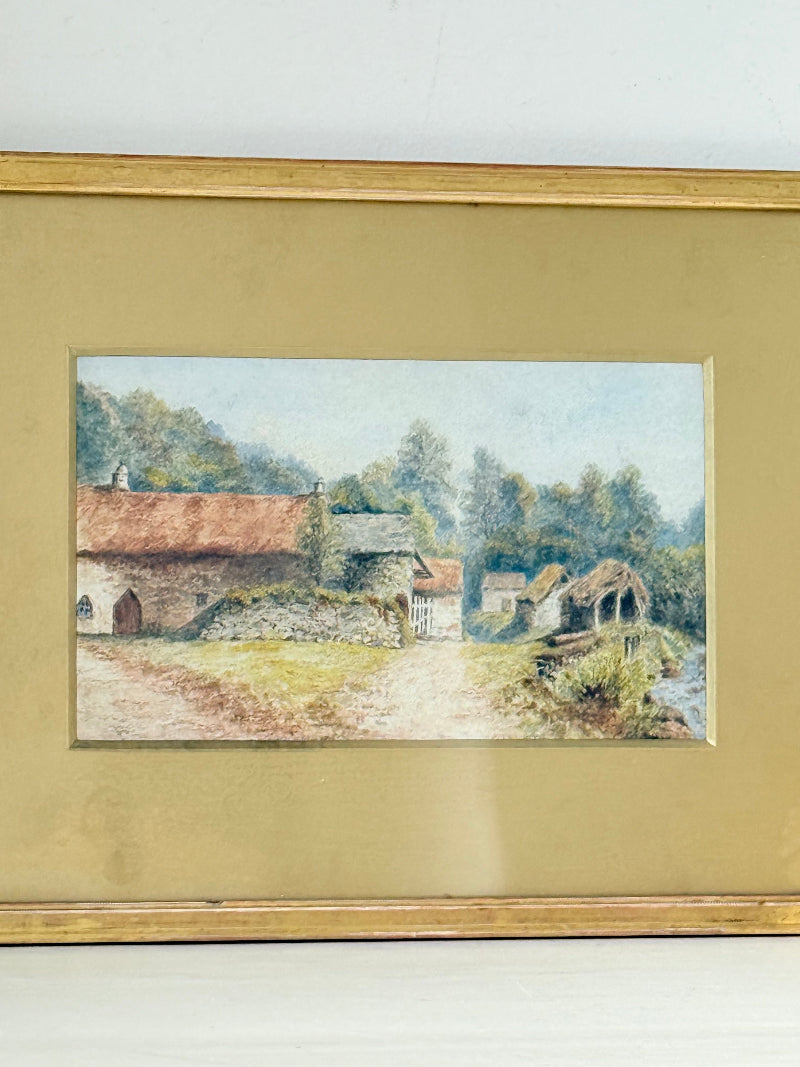 Framed vintage watercolour of countryside farm buildings with red roofs in gold frame photographed on a white surface