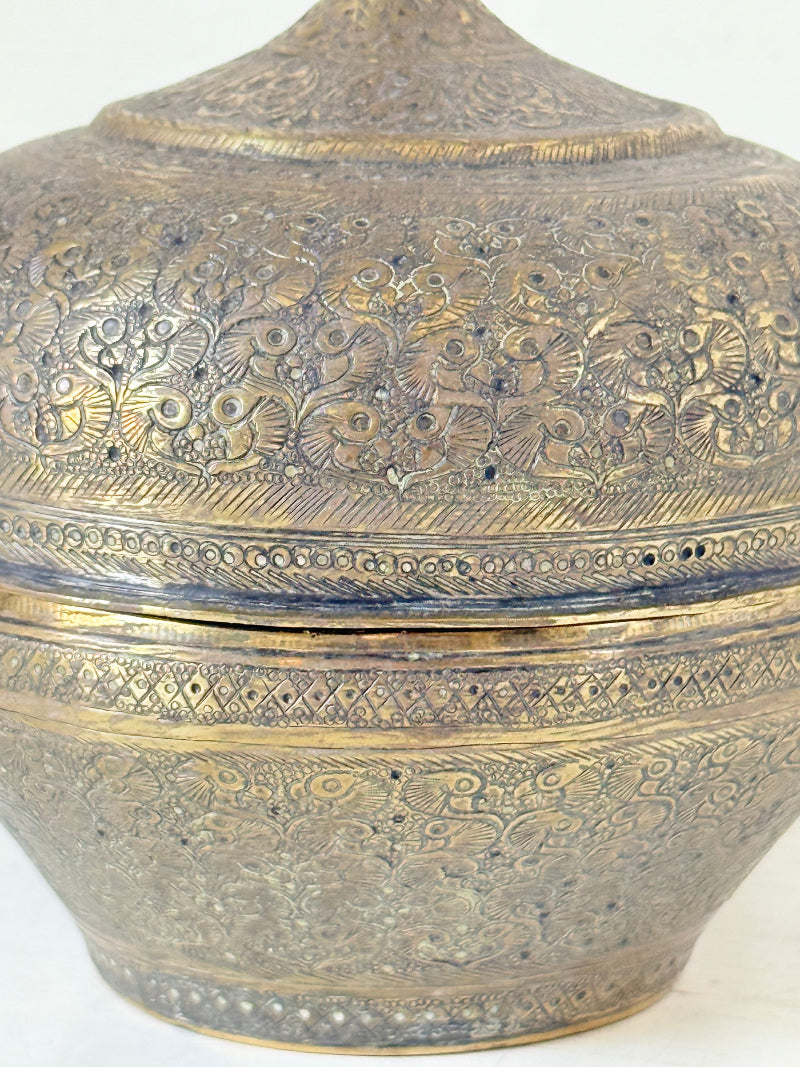 Indian Benares brass lidded jar with pointed finial and darkened interior, photographed on a white surface
