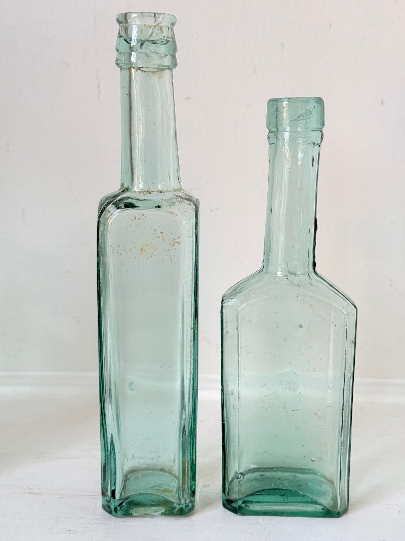 Set of five antique aqua green glass bottles with embossed lettering, photographed on a white surface